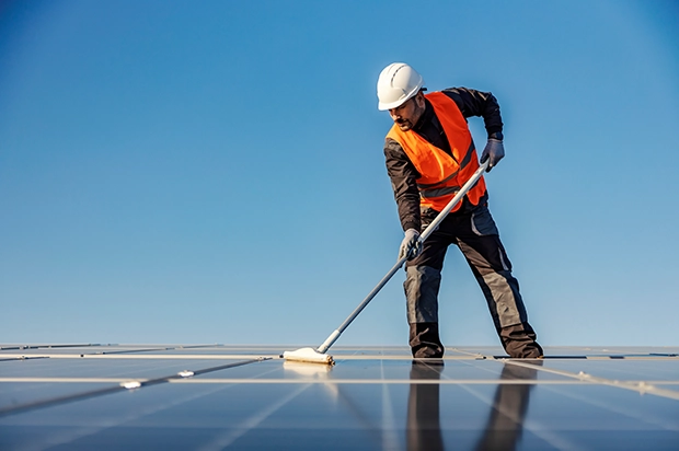 Technician spraying water to clean rooftop solar panels under bright sunlight